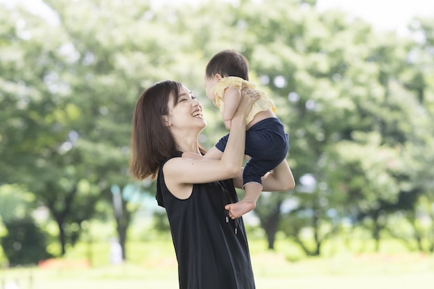 녹색 공원에서 아기를 들고 아시아 젊은 엄마 | 프리미엄 사진